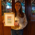 Artist happily holding their framed print of their contemporary stylised version of the tulip and blue bird stained glass windows featured in the background where they took the photo.