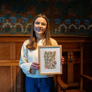 Artist Tiana McInerney holding her rowan berry frieze inspired illustrated artwork in front of the hessian wall feature and handcrafted wooden furniture in the Dining Room at Blackwell – the Arts & Crafts house.