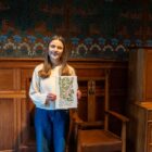 Local artist Tiana McInerney happily holding her rowan berry inspired print in front of the hessian wall-covering in the Dining Room.