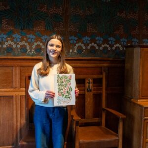 Local artist Tiana McInerney happily holding her rowan berry inspired print in front of the hessian wall-covering in the Dining Room.