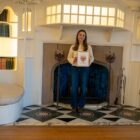 Artist Tiana McInerney in front of the grand inglenook fireplace in the White Drawing Room with her framed fire dog inspired illustration.
