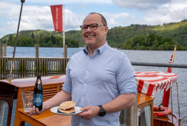 Matt Hicks, Catering Manager, holding breakfast bap and bottle of locally brewed beer on Osprey.