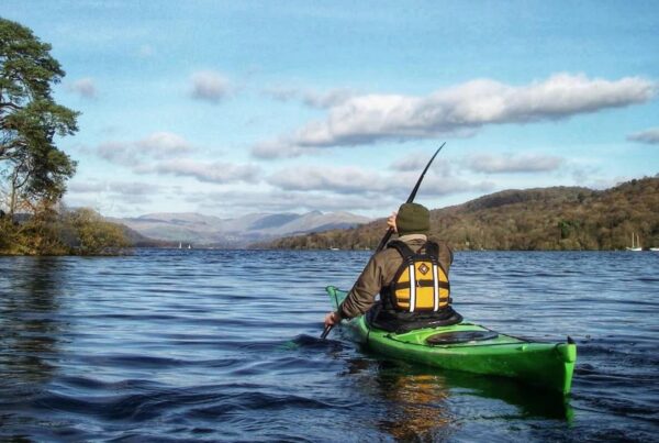 Person in a green canoe paddling across the lake on a beautiful sunny day.