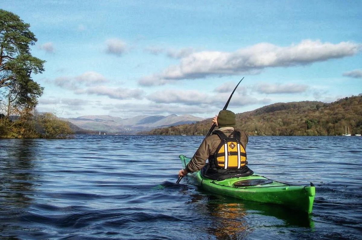 Person in a green canoe paddling across the lake on a beautiful sunny day.